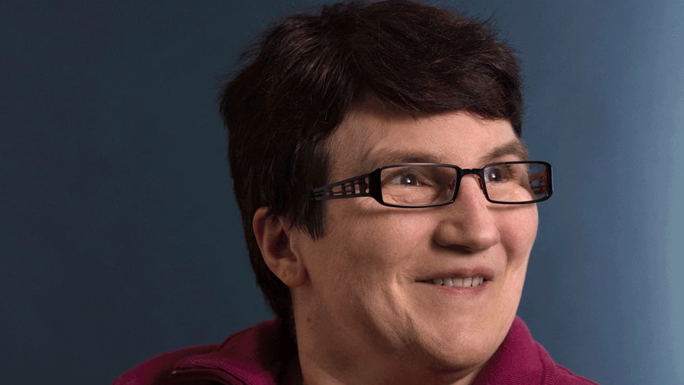 Portrait d'une dame aux cheveux bruns et aux lunettes souriantes.