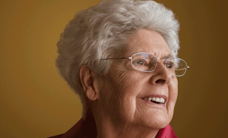 Portrait d'une vieille dame aux cheveux blancs et aux lunettes qui sourit.