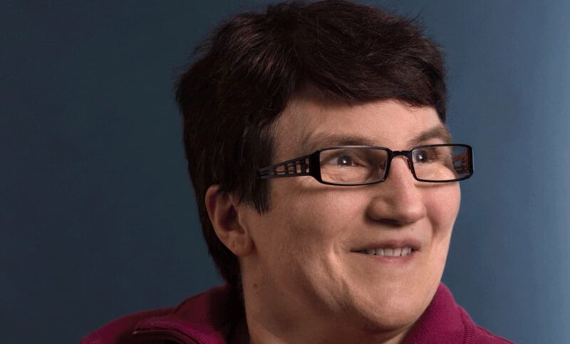 Portrait d'une dame aux cheveux bruns et aux lunettes souriantes.